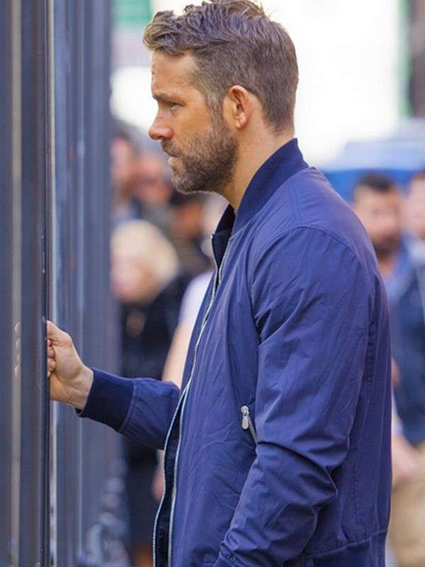 Man in a blue jacket standing next to a glass door with a blurred background